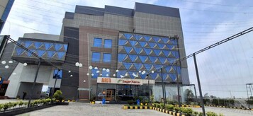 Un edificio moderno con fachada de vidrio, un letrero que dice 'BARISTA Sugar Ratha' y un área exterior bien cuidada con plantas en macetas.