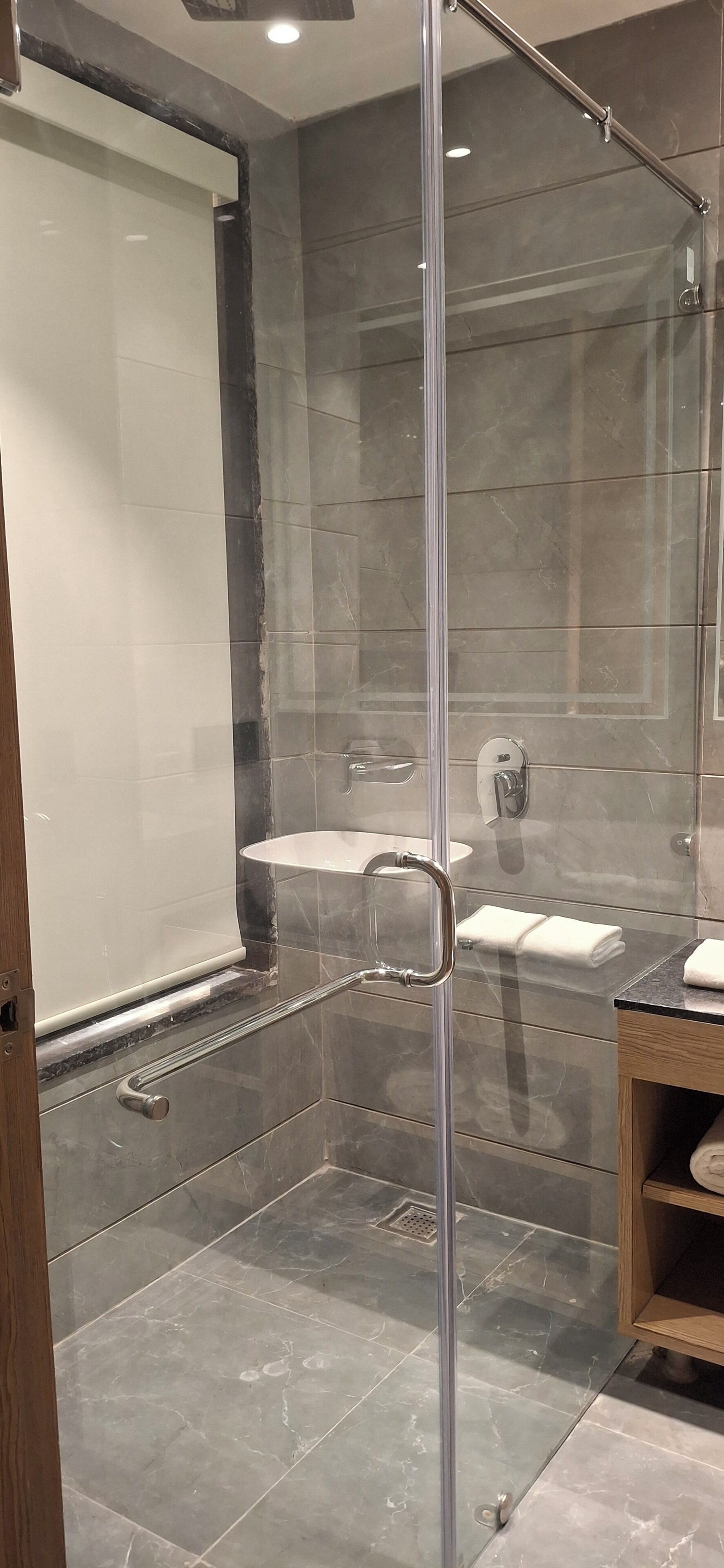A modern bathroom with a glass-enclosed shower, a white sink, and a wooden vanity.