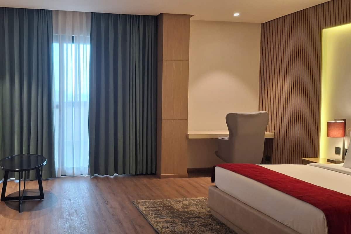 Ein Hotelzimmer mit einem Bett, zwei Sesseln, einem kleinen Tisch und einem Nachttisch mit Lampen.