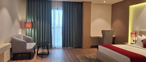 A hotel room with a bed, two armchairs, a small table, and a nightstand with lamps.