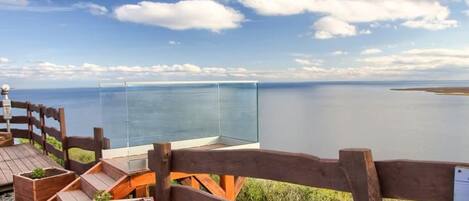 A wooden deck with a glass viewing platform overlooking a body of water.
