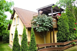 Une maison à deux étages, avec un toit en tuiles, une véranda en bois et une clôture en bois.