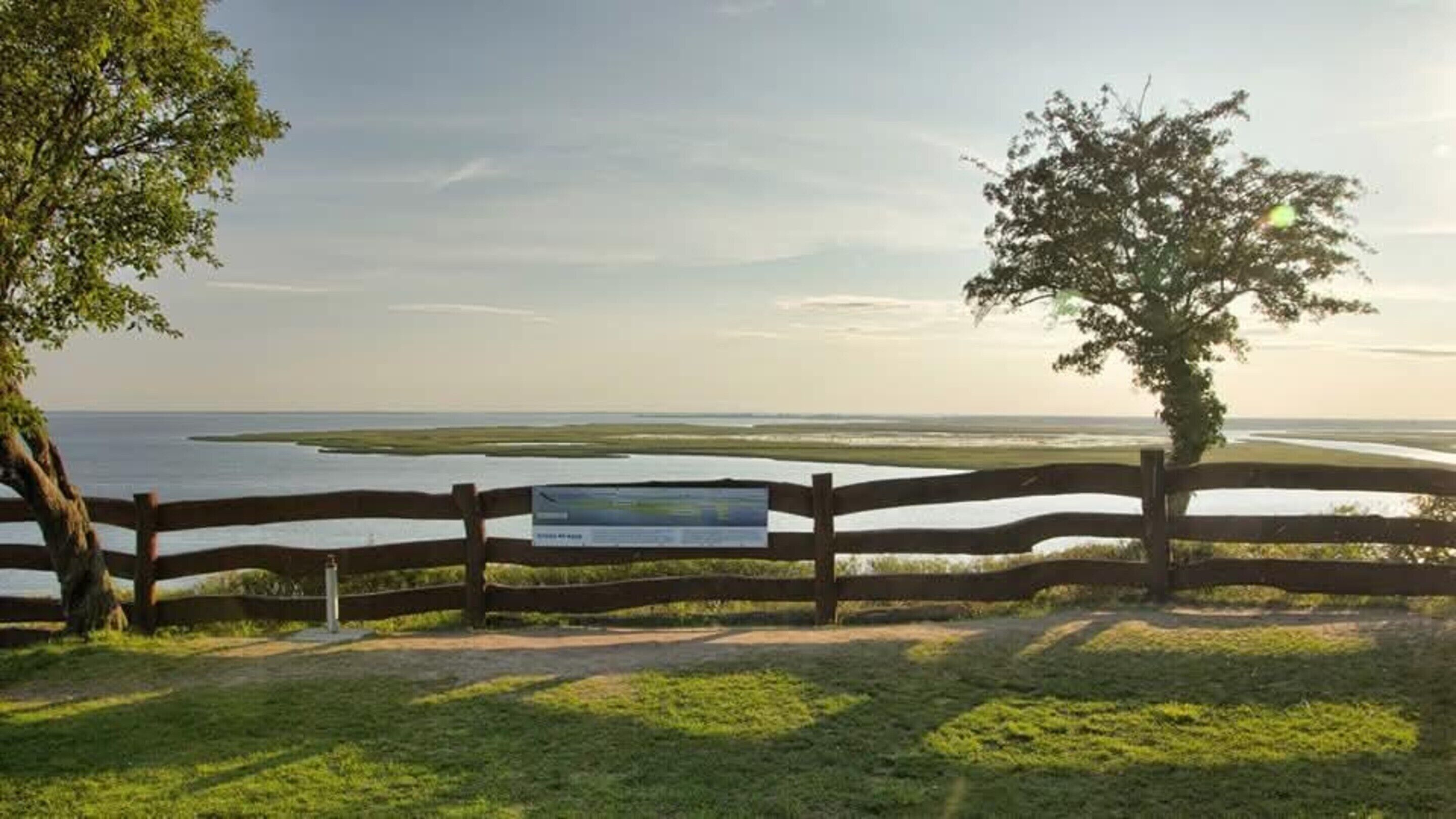 A wooden fence with a sign, a grassy area, and a view of a water body.