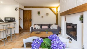 Una sala de estar acogedora con un sofá, una mesita de centro y una chimenea. Hay una zona de cocina con un microondas y una puerta de madera.