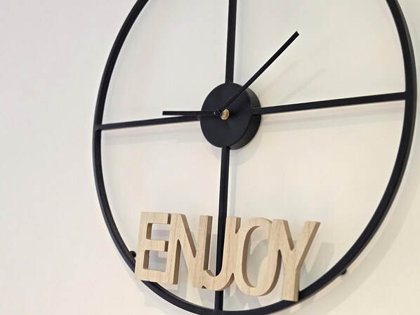 Un reloj de pared de diseño minimalista, con marco negro y letras de madera que dicen 'ENJOY'.