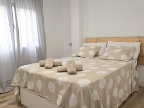 A neatly made bed with a polka dot bedspread, a wooden headboard, and a window with sheer curtains.