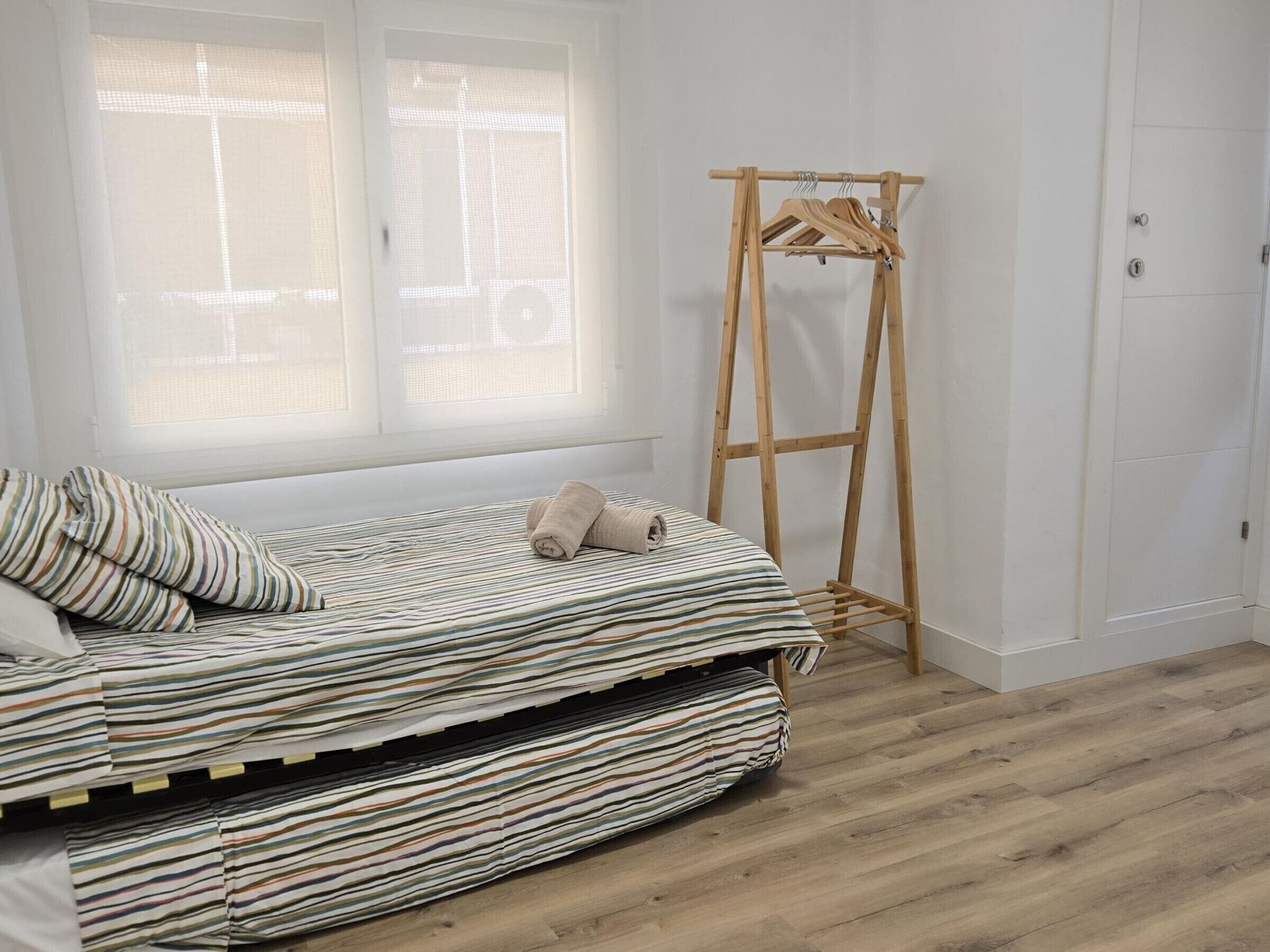 Ein Schlafzimmer mit einem Bett, einem Wäscheständer aus Holz und einem Fenster.