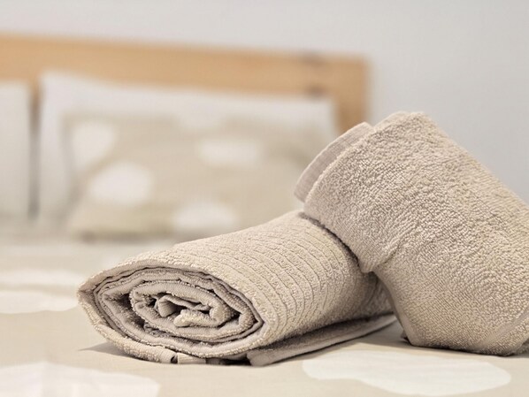 A neatly folded beige towel on a bed with a wooden headboard and a white pillow with a circular pattern.