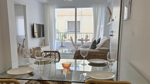 A dining area with a glass table, wicker chairs, and a view of a balcony with a sofa and a table.