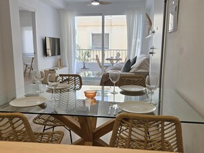 A dining area with a glass table, wicker chairs, and a view of a balcony with a sofa and a table.