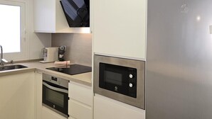 A modern kitchen with white cabinetry, a stainless steel refrigerator, a built-in oven, a microwave, and a coffee maker.