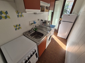 A compact kitchen with a sink, washing machine, and a refrigerator. - Collioure T2 Apartment with Terrace and Parking (Collioure)