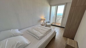 A bedroom with a bed, a nightstand, a lamp, and a view of the sea through a sliding door. - 2-room apartment with sea-facing balcony - Saint-Hilaire-de-Riez (Saint-Hilaire-de-Riez)
