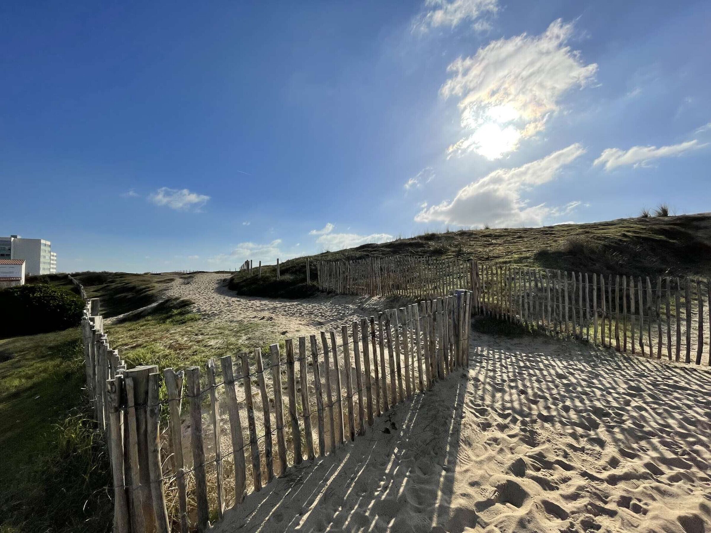 Ein Sandstrand mit Holzzäunen und einem Gebäude im Hintergrund.