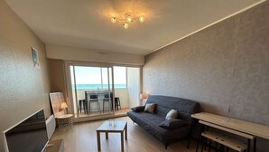 A modern living room with a sofa, a small table, a TV, and a balcony with a view of the sea. - 2-room apartment with sea-facing balcony - Saint-Hilaire-de-Riez (Saint-Hilaire-de-Riez)