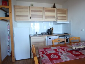 Cozinha compacta com armários de madeira, geladeira, pia, fogão e mesa de jantar com toalha de mesa vermelha e branca.