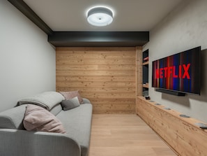 Un salon moderne avec un canapé gris, un mur recouvert de panneaux en bois et un téléviseur fixé au mur qui affiche le logo de Netflix.