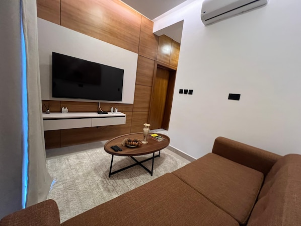 Una sala de estar moderna con un televisor de pantalla plana, armarios de madera, una mesa de centro redonda y un sofá marrón.