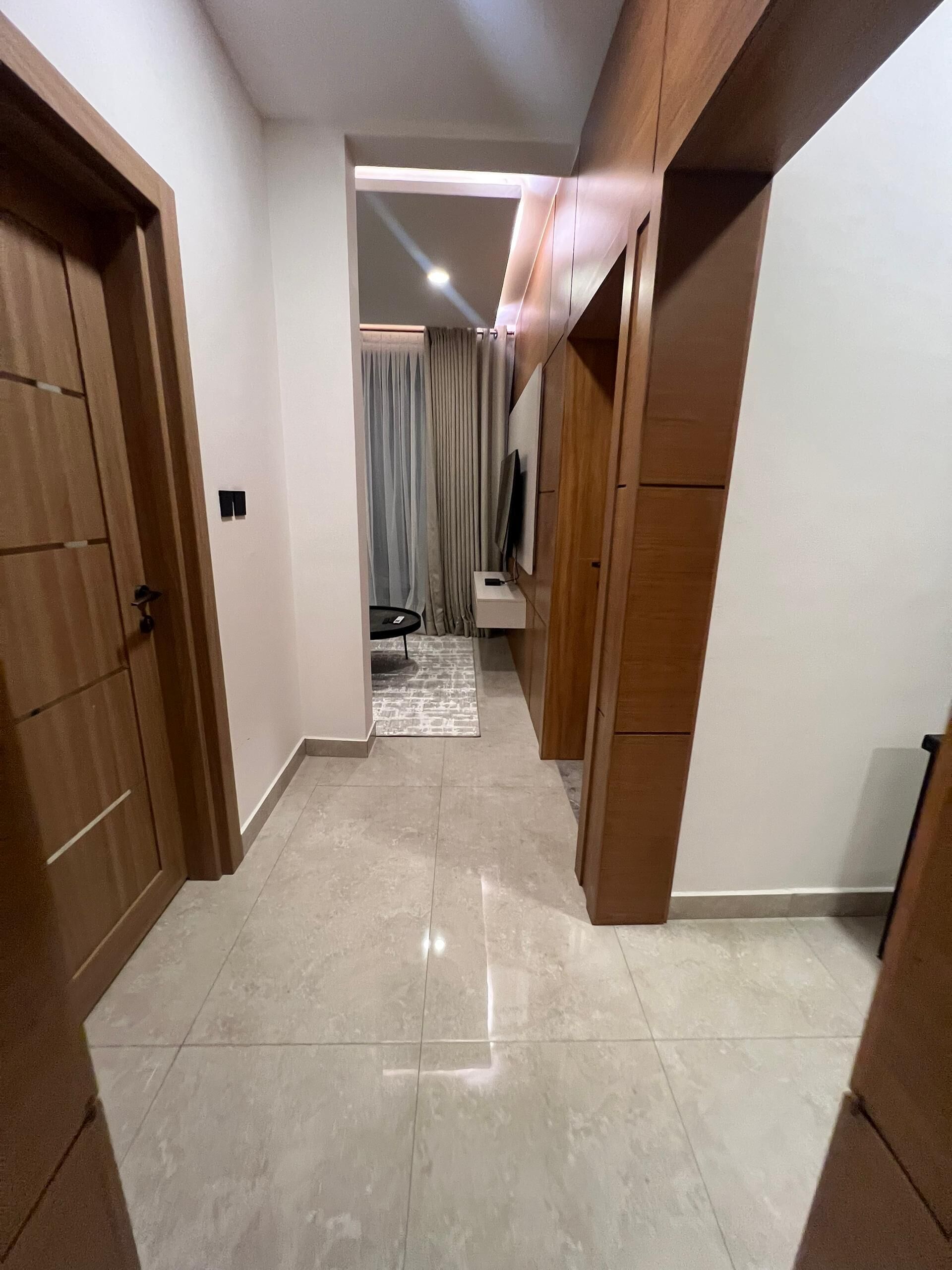 Un pasillo con piso de baldosas, puertas de madera y una pequeña mesa con una silla.