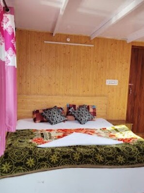 Een kamer met een houten hoofdbord, een bed met beddengoed met een patroon, en een roze gordijn.