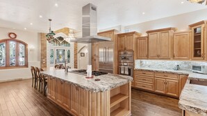 A spacious kitchen with wooden cabinets, a large island, stainless steel appliances, and a chandelier. - Broadmoor Retreat Luxe European Style Hot Tub (Colorado Springs)