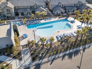 Une piscine entourée de chaises longues, de palmiers et d’une clôture, avec des immeubles d’habitation en arrière-plan.