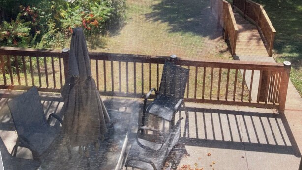 Une terrasse dotée de mobilier d’extérieur, d’un barbecue et offrant une vue sur un jardin avec une maison et des arbres.