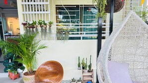 A cozy outdoor seating area with a woven chair and a cushioned hanging seat, surrounded by various potted plants and a tiled floor. - Belvilla Chiangmai near Lanna Hospital (Chiang Mai)
