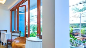 A dining area with wooden chairs, a round table, and a view of the outdoors through large glass doors. - Belvilla Chiangmai near Lanna Hospital (Chiang Mai)