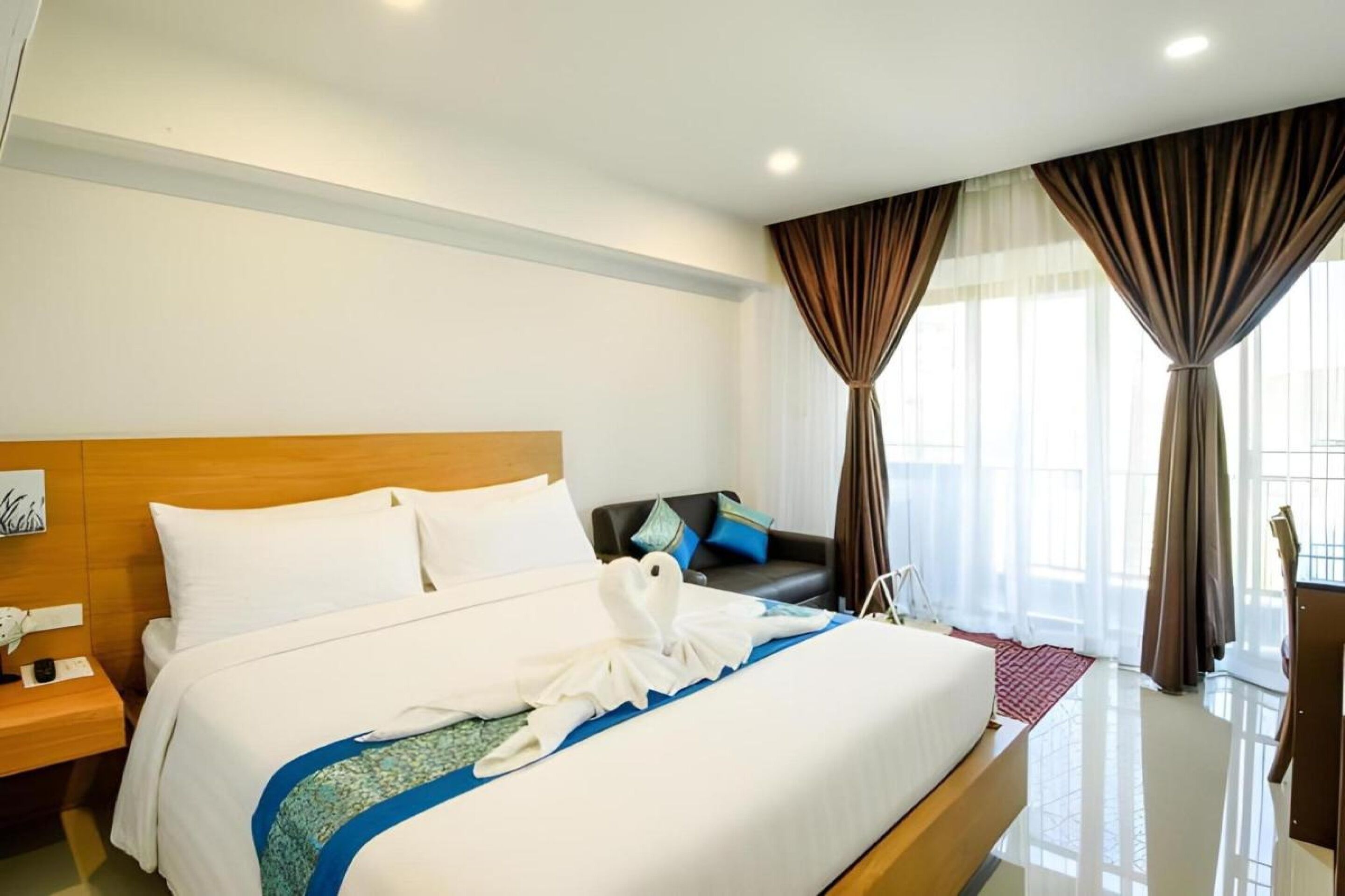 A hotel room with a large bed, a wooden headboard, a nightstand, a desk, and a chair.