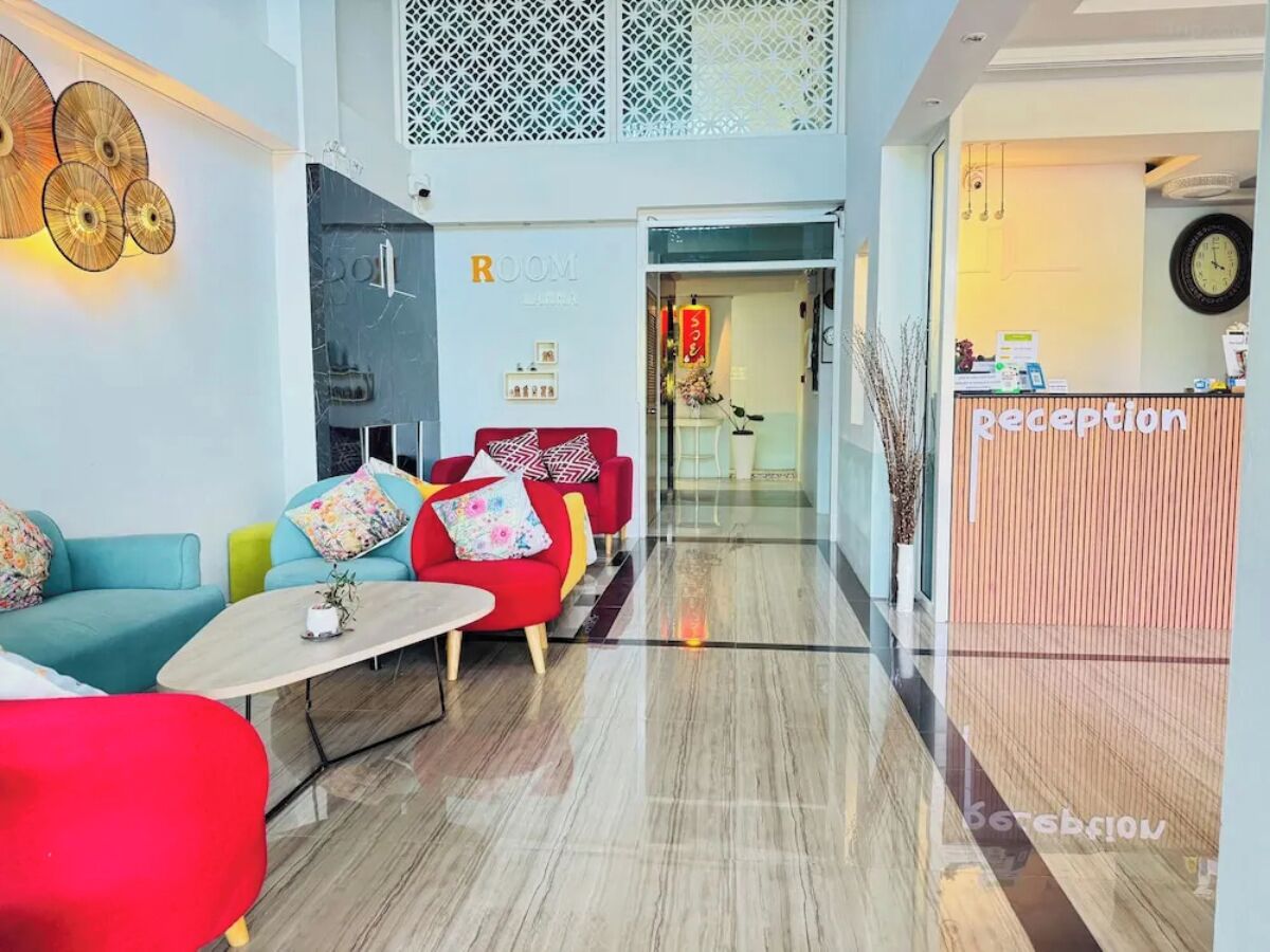 Eine moderne Hotellobby mit einer Rezeption, einem roten Sofa, einem türkisblauen Sofa und einer Kaffeemaschine.