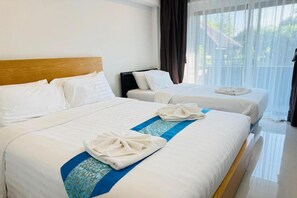 Quarto de hotel com duas camas, cabeceira de madeira, roupa de cama branca e vista para o verde através de cortinas translúcidas.