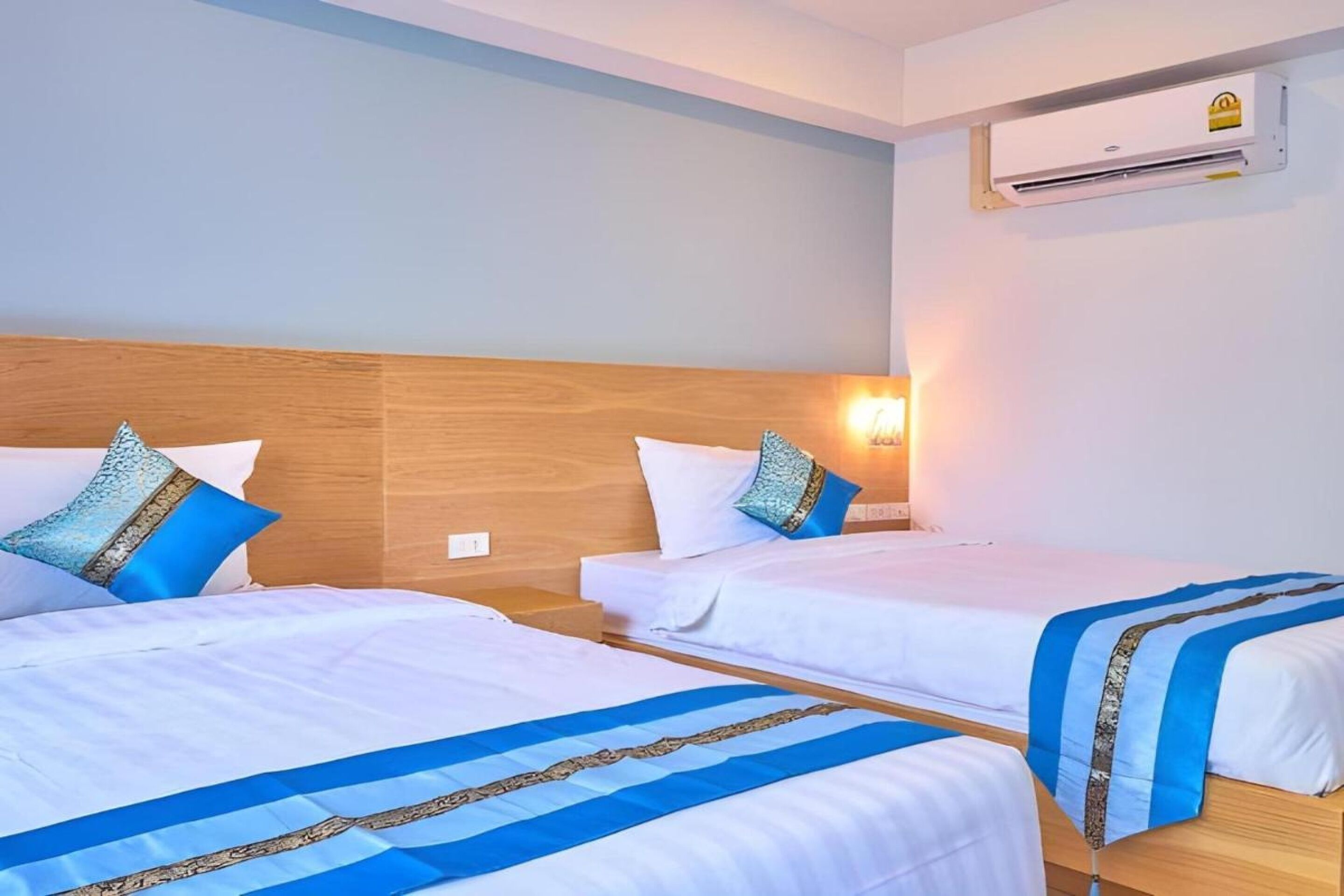 Ein Hotelzimmer mit zwei Einzelbetten, jeweils mit einer blau-weißen Bettdecke und einem Holzkopfteil.