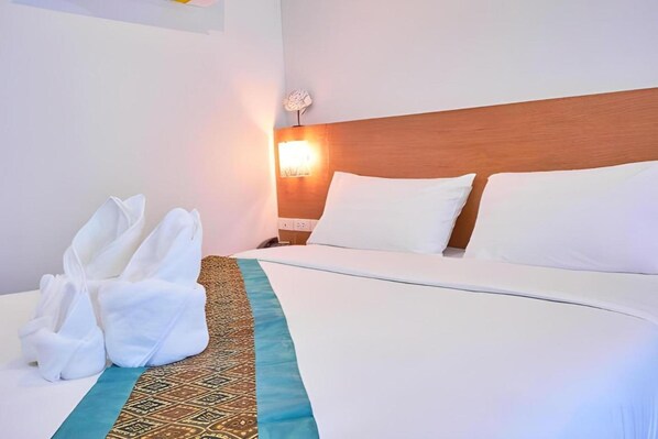 A hotel room with a neatly made bed, a headboard, a wall-mounted lamp, and a pair of towels on the floor. - Belvilla Chiangmai near Lanna Hospital (Chiang Mai)