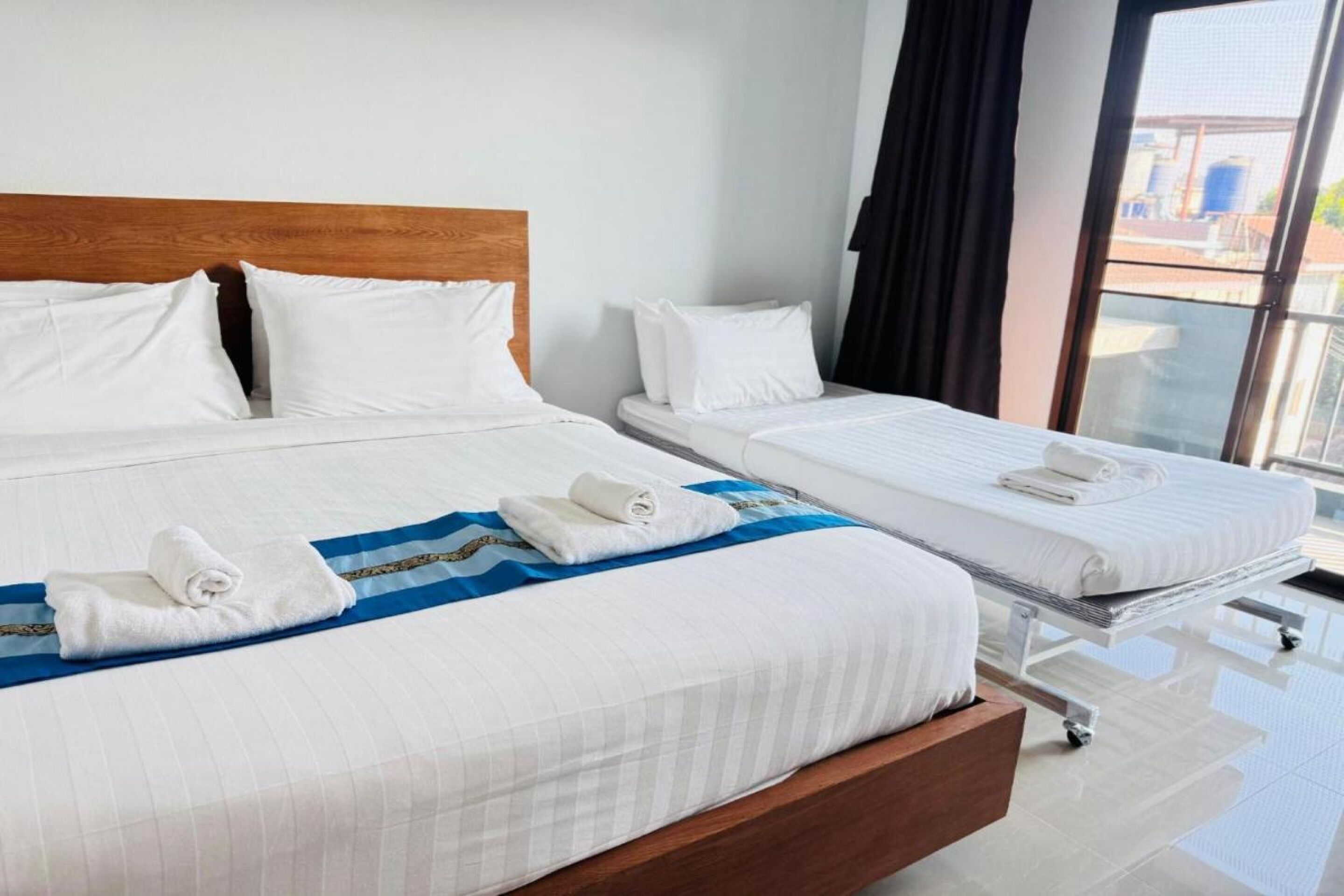 A hotel room with two beds, a wooden headboard, white bedding, and a view through a large window.