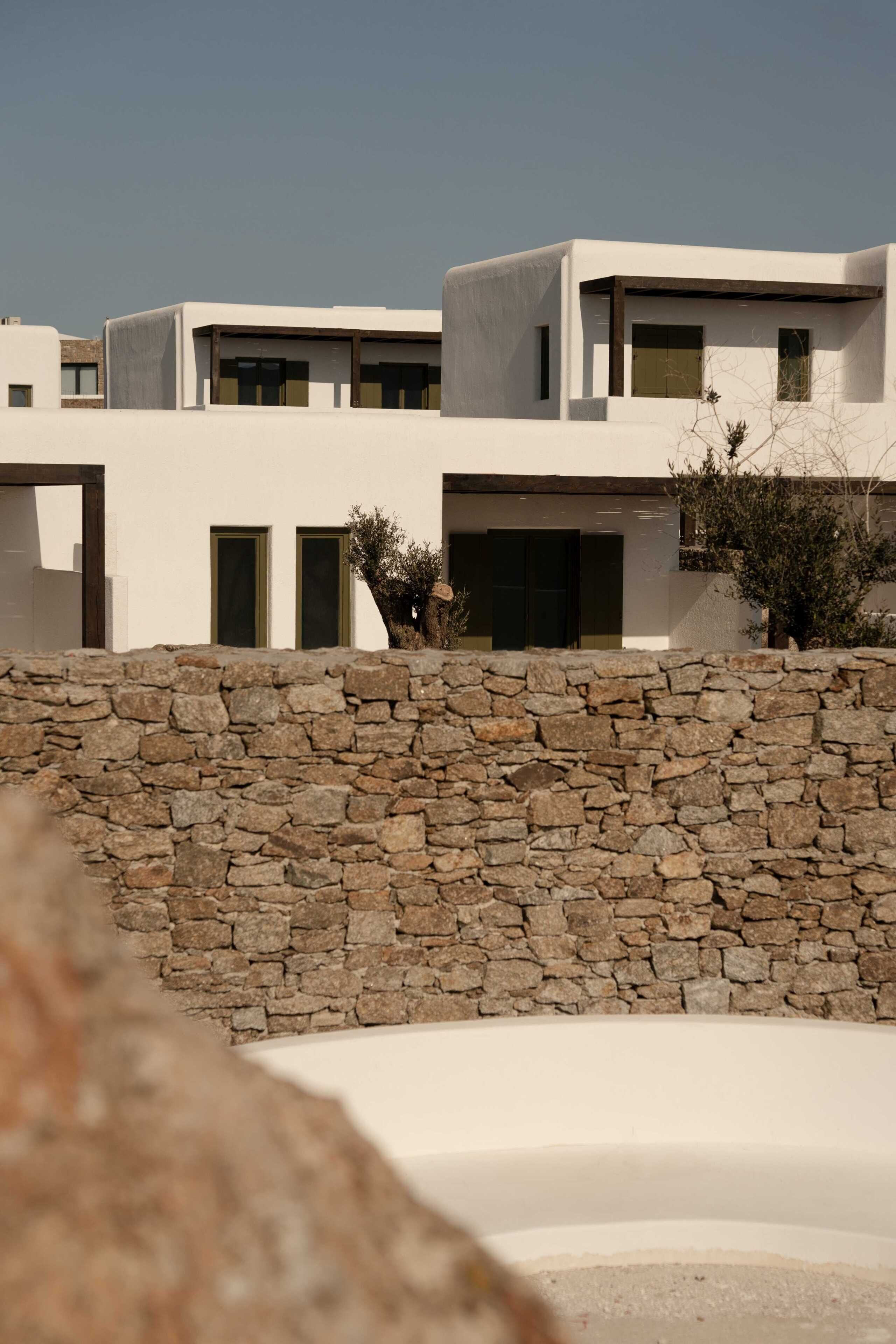 Un edificio moderno con un muro de piedra al frente, estructuras de techo plano y un cielo despejado.