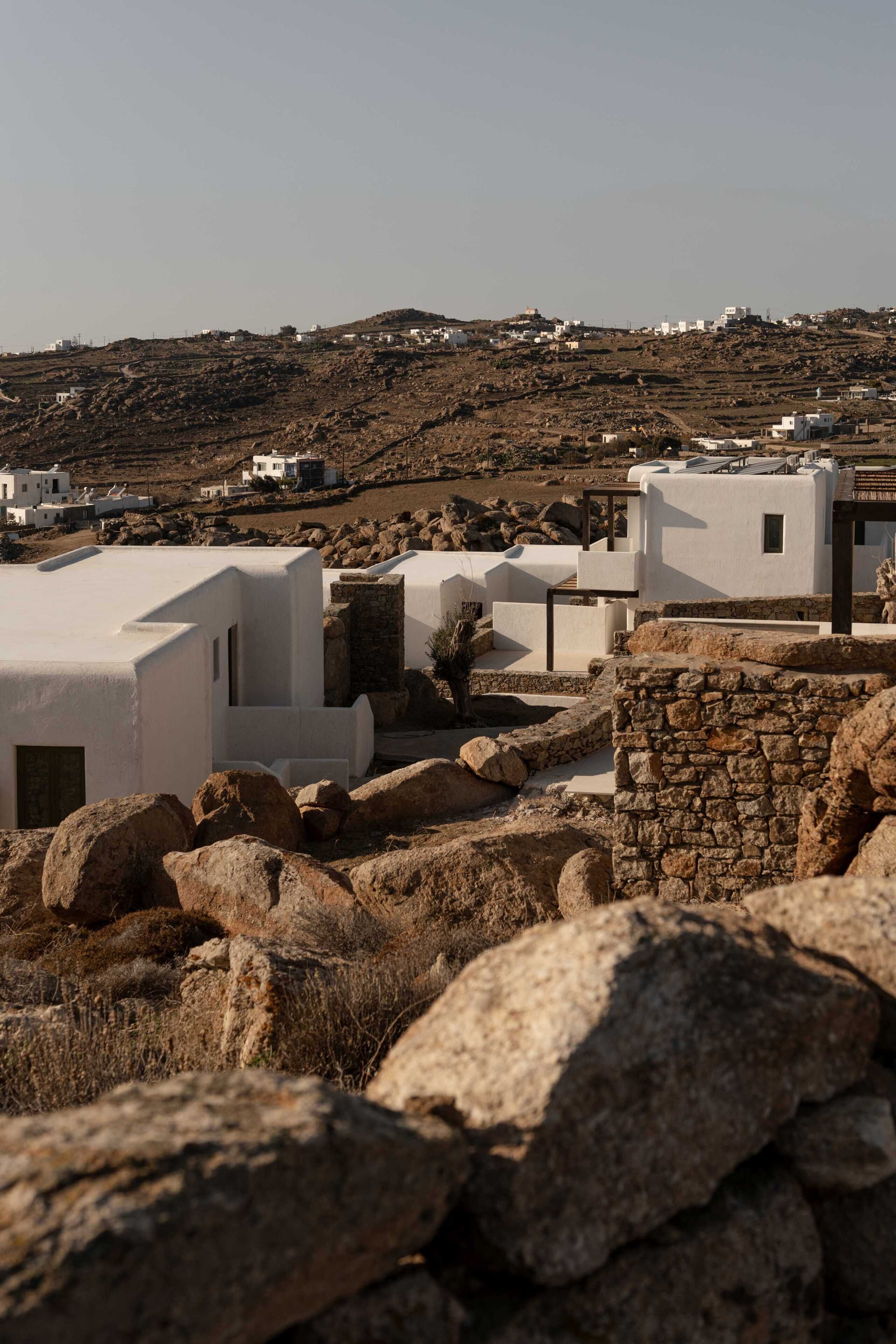 A white building with a flat roof, surrounded by large rocks and a stone wall.