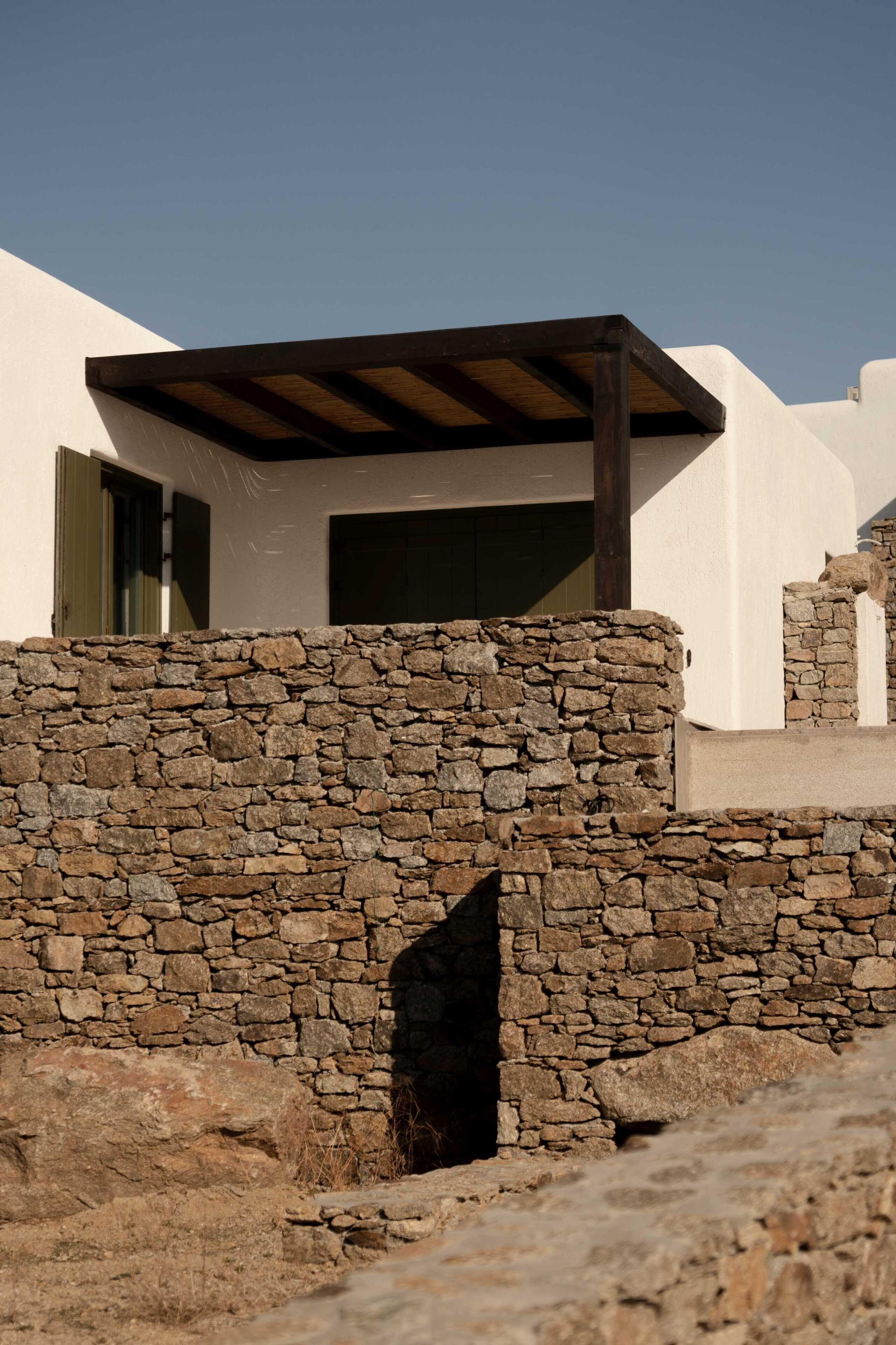 A stone wall with a doorway leading to a building with a wooden pergola.