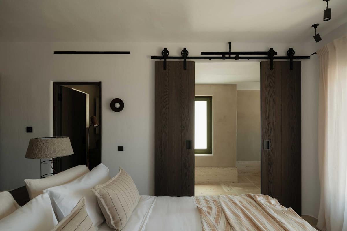 A bedroom with a bed, a lamp, a door, and a window.