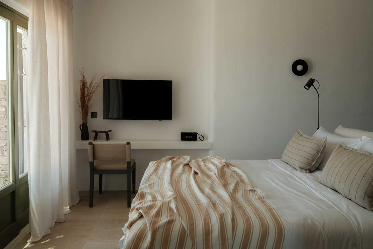 A bedroom with a bed, a chair, a TV, a lamp, and a window with curtains.