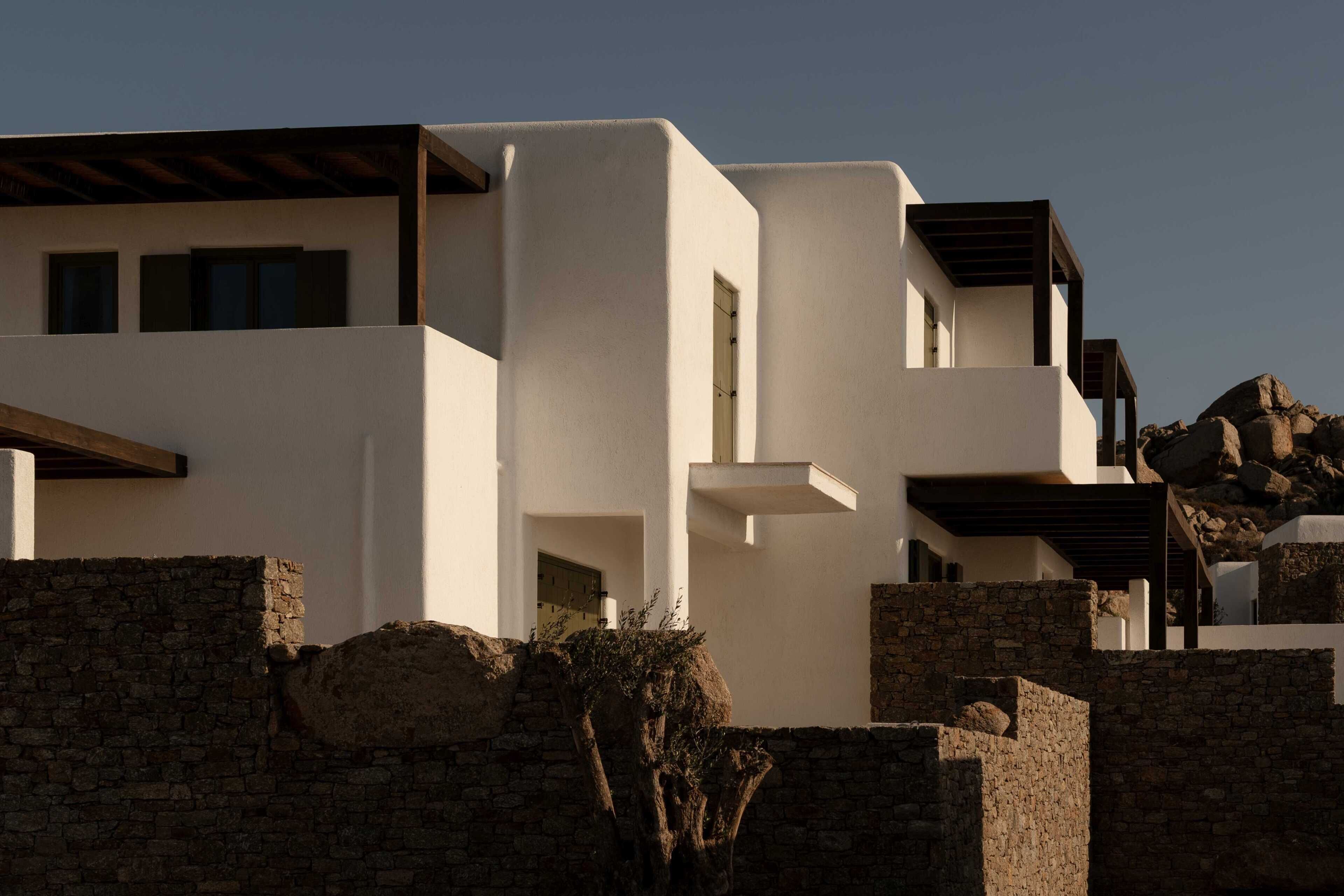 Un edificio moderno con techo plano, varias ventanas y un muro de piedra en primer plano.