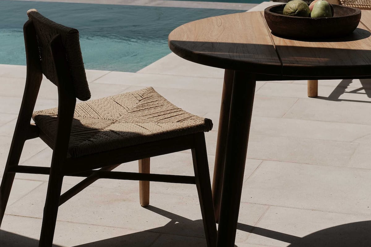 A table with a bowl of fruit, a wicker chair, and a view of the sea and rocky landscape.