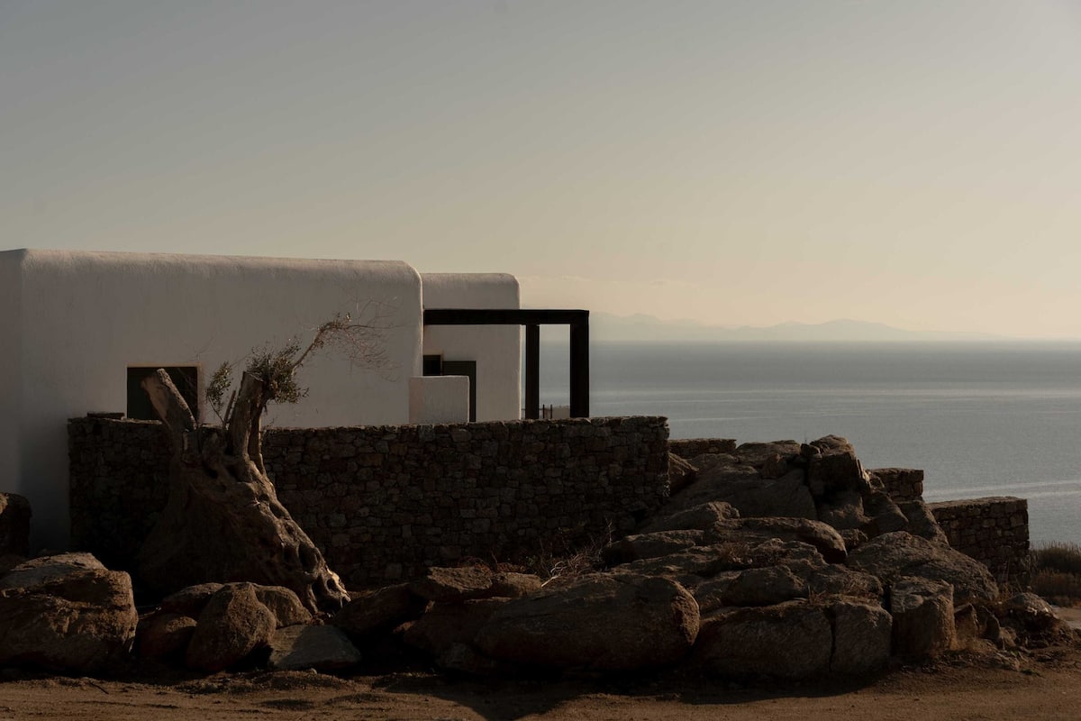 A coastal building with a stone wall, a tree, and a view of the sea.