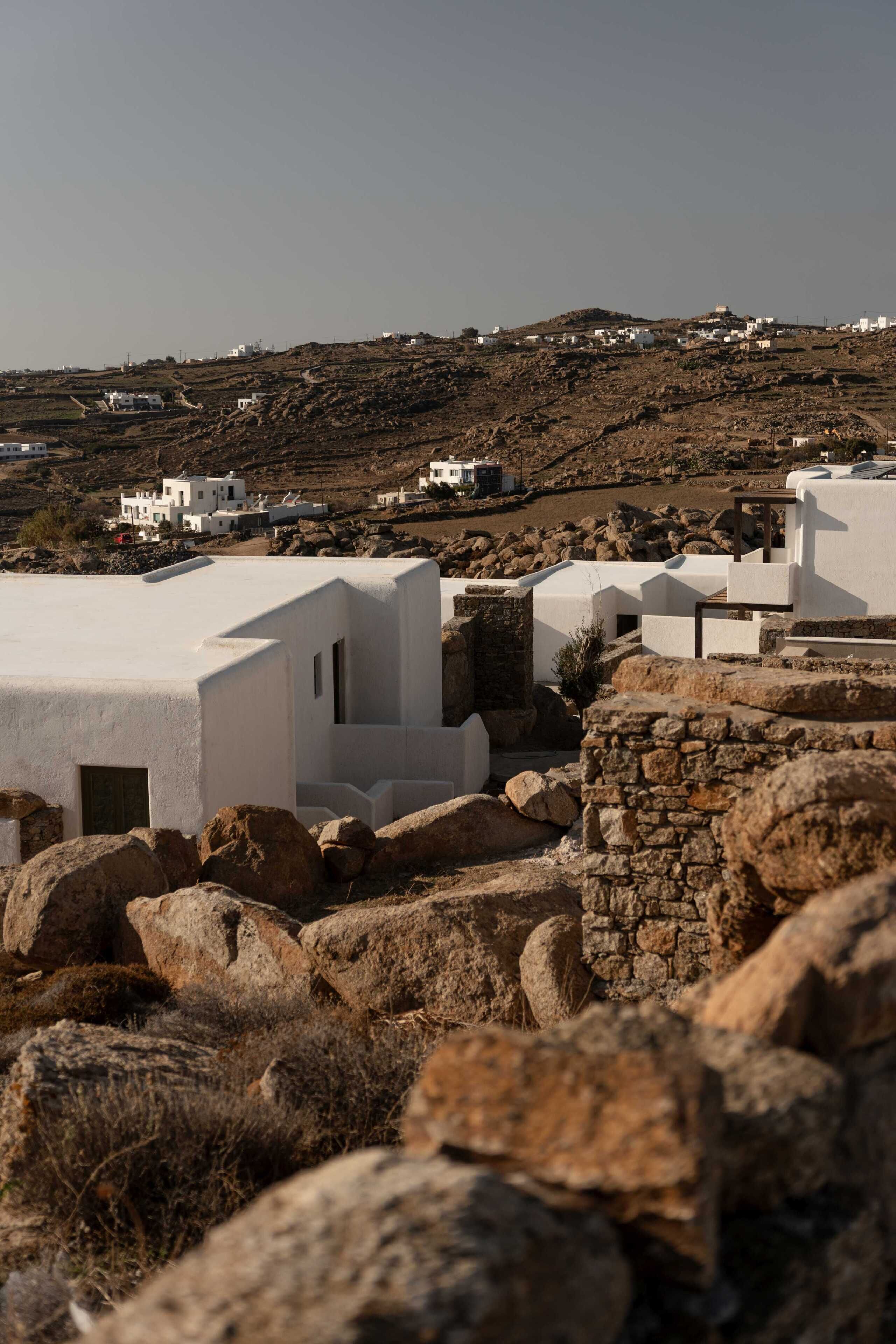 A white building with a flat roof, surrounded by large rocks and dry vegetation.