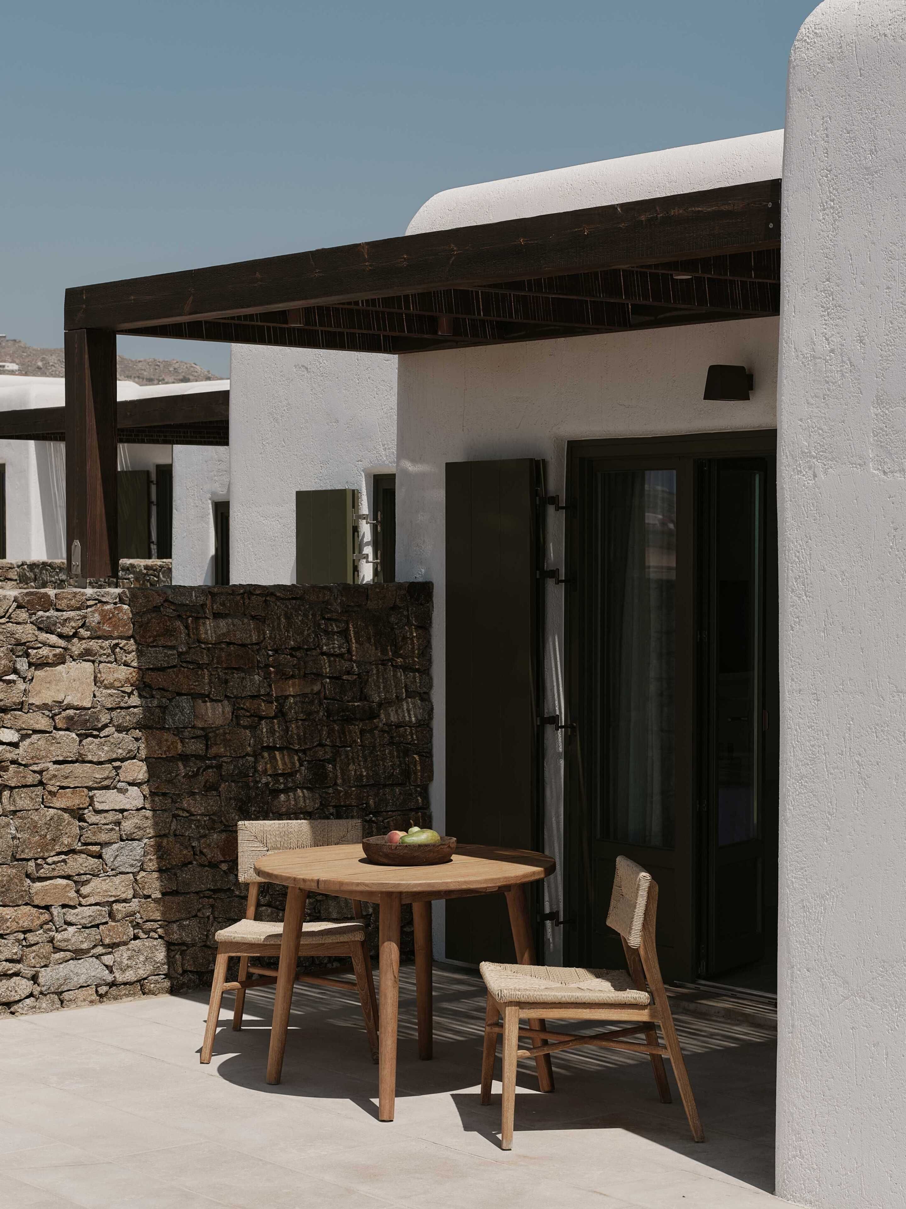 Eine Terrasse mit einem runden Holztisch und Stühlen, einer Steinmauer und einer Tür.