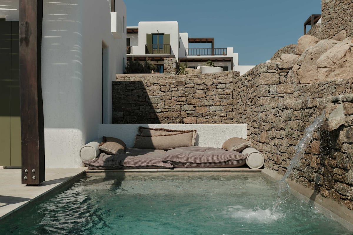 A pool area with a stone wall, a white building, and a wooden deck.