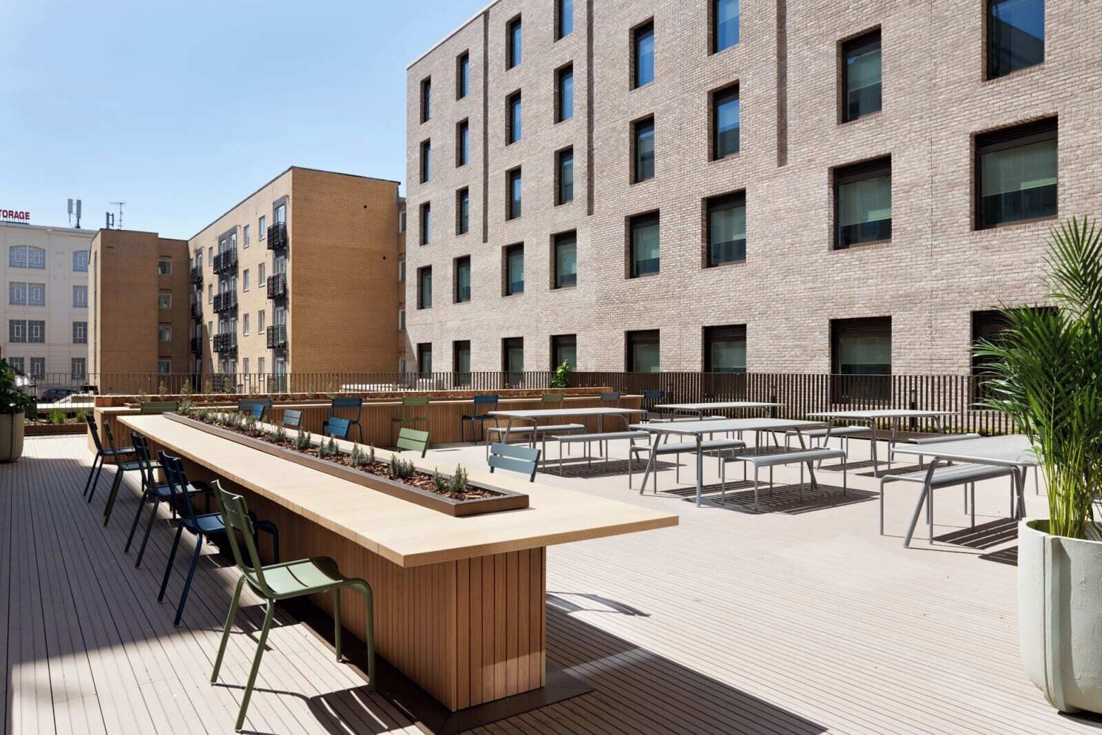 Eine Dachterrasse mit Sitzgelegenheiten im Freien, einem langen Tisch und einem Blumentopf.