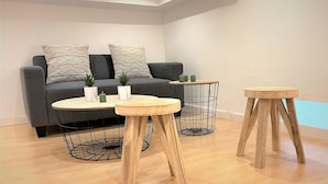 En moderne stue med en grå sofa, to runde træborde med metalwire-stel og et lille rundt bord med træ- og metalwire-stel.