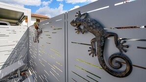 Una pared de metal con una escultura decorativa de lagarto y una serie de hendiduras horizontales.