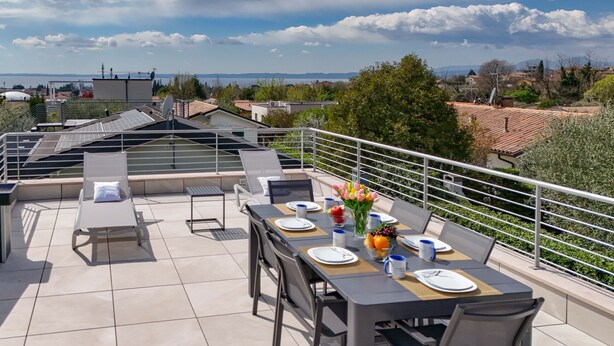 Una terraza en la azotea con una mesa de comedor preparada para cuatro personas, rodeada de sillas y un sofá.